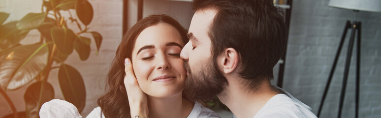 handsome bearded man kissing beautiful smiling woman at home