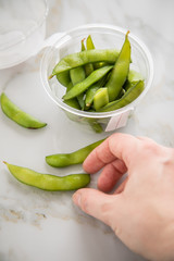 Frau isst portion grüne, japanische Edamame Sojabohnen in Plastik Lieferdienst Take Away Schale