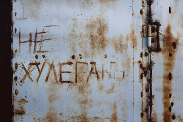 Old rusty iron wall with scratched "Don't hooligan" inscription in Russian. The surface is partially painted blue. Perfect for background and grunge design.