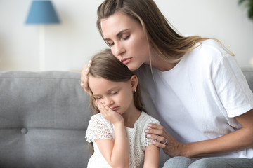 Loving mother embracing, comforting upset little daughter close up
