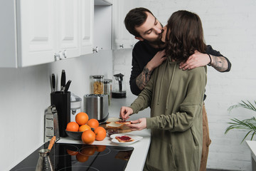 beautiful young couple kissing while preparing toasts during breakfast in kitchen