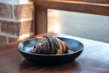A piece of chocolate croissant in a black plate on wooden table in bakery shop