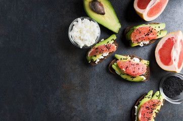 Top view of served sandwiches with avocado,cheese,grapefruit on grey table in the kitchen