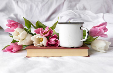 white and pink tulips, mug on the book, white sheet, bouquet of tulips