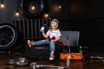Fototapeta na wymiar child laughs merrily in a car repair shop among tires and wheels holding a bottle of clean drinking water