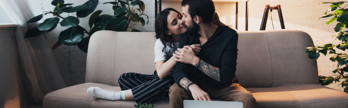 beautiful young tattooed couple embracing while sitting on couch in living room