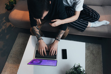 cropped view of couple sitting ang hugging while using laptop with web shopping website on screen at home