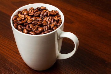 Roasted Coffee beans in a white mug cup isolated on a rustic wood table 