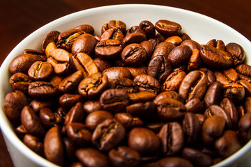 Roasted Coffee beans in a white mug cup isolated on a rustic wood table 
