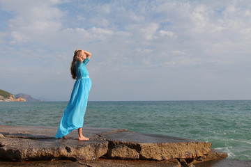 pregnant girl in blue dress on stones by the sea