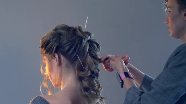 Makeup artist and hairdresser are preparing bride before wedding. Hairdresser-stylist with short stylish hairstyle applies makeup, makes false eyelashes, paints lips, curls girl, spectacular lighting