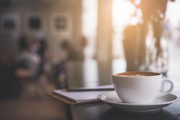 Cappuccino cup on the table with blur people in coffee shop background, vintage tone 
