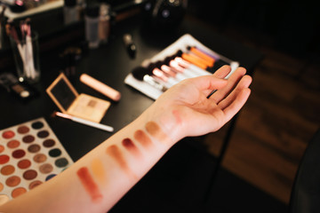 Woman's hands with eyeshadow examples on skin. Colorful palette. Brushes blush and mirror on table. Cut view. Close up.
