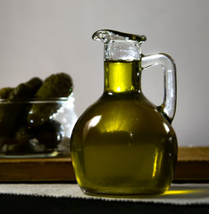 Glass jar with olive oil and marinated cucumbers on the table
