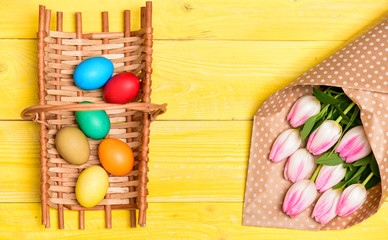 Colorful bright eggs and bouquet fresh tulip flowers on yellow background top view. Spring holiday. Tradition celebrate easter. Happy easter season. Easter eggs symbol. Spring vibes. Easter is coming
