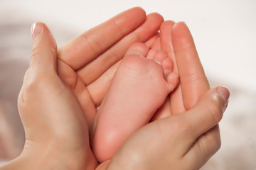 the mother holds the feet of her little baby in her palms