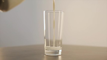 Glass of spilling milk. Milk is poured past the glass. Beautiful glass tumbler on a gray table. View from above. - Powered by Adobe