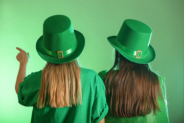 Young women in green hats on color background. St. Patrick's Day celebration