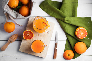 Glass of fresh pressed orange juice and blood oranges on wooden table. Bright summer mood. Top view