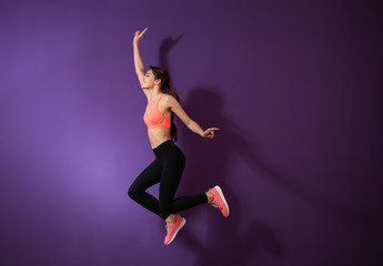 Sporty young woman jumping against color background