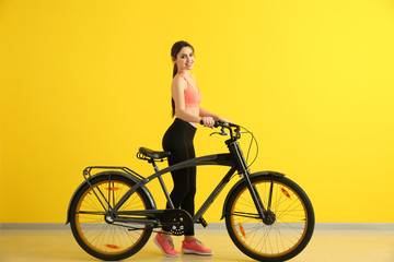 Sporty young woman with bicycle near color wall