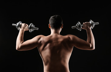 Sporty young man training with dumbbells against dark background