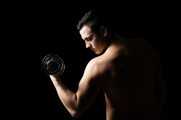 Fototapeta na wymiar Sporty young man with dumbbell against dark background