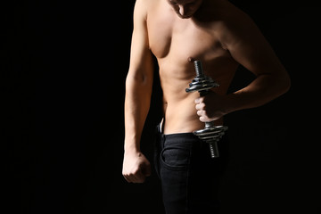 Sporty young man with dumbbell against dark background