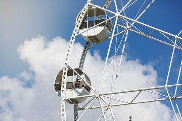 fragment of a ferris wheel against a blue sky with clouds, concept