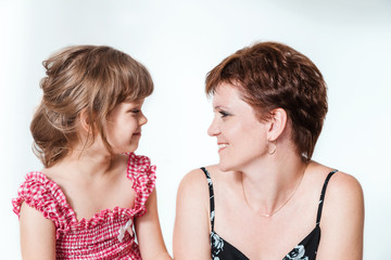 happy mother and daughter look at each other on white background. Thirty-year-old woman and six-year-old daughter