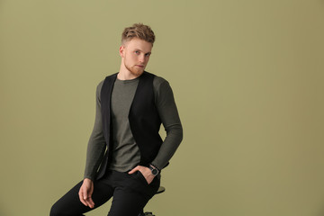 Fashionable young man sitting on stool against color background