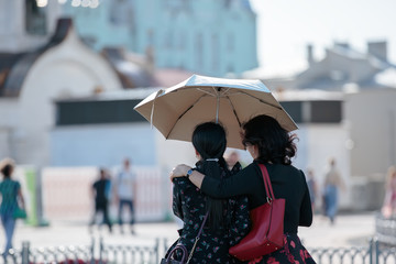 Two girls stand embracing under an open umbrella and look at the city