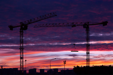 Sunset on the construction site. Silhouettes of workers and two cranes.
