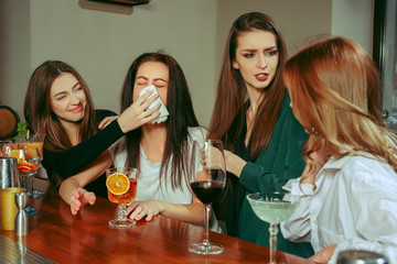 Stress. Female friends having a drinks at bar. They are sitting at a wooden table with cocktails. They are wearing casual clothes. Friends comforting and soothing a crying girl - Powered by Adobe