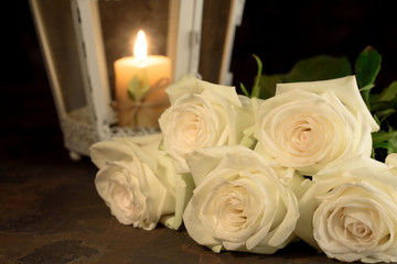 Beautiful white roses and candle on table against black background