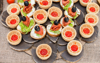 Sandwiches with salami and olives, baskets of red caviar on a wooden plate