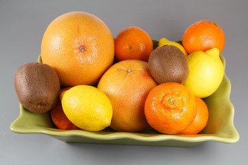 Dish of citrus with clementines, grapefruits, lemons and kiwis on a table