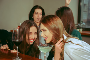Female friends having a drinks at bar. They are sitting at a wooden table with cocktails. They are wearing casual clothes.