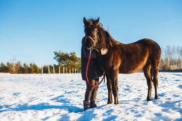 Girl embraces arab black horse. Winter snowy field on a sunny day