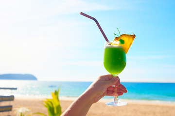Taking cocktail in hand. Summer landscape on sunny day is on the background.