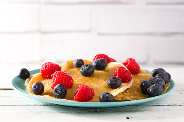 Pancakes with raspberries, blueberries and honey on white wooden table.