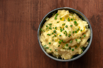 Pomme puree, a bowl of mashed potatoes with scallions and thyme, shot from above on a dark rustic wooden background with copy space