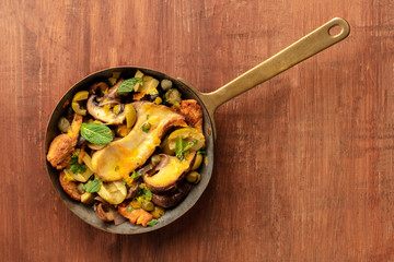 An overhead photo of a rustic mushrooms and olives saute with mint in a cast iron pan, on a dark rustic background with a place for text