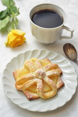 A cookie with pineapple on a white saucer. Coffee in a cup on a white background
