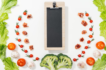 top view of clipboard among tomatoes, lettuce leaves, prosciutto, broccoli and garlic