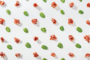 top view of delicious prosciutto near green basil leaves on white background