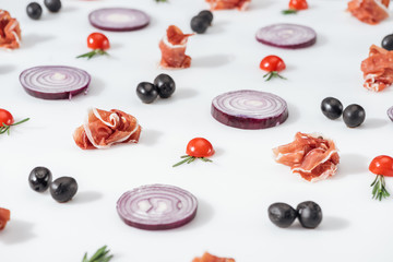 selective focus of red onions near prosciutto, cherry tomatoes with rosemary twigs and black olives  on white background