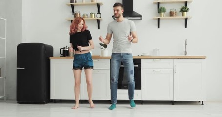 Happy young couple dancing in kitchen wearing pajamas listening to music morning at home