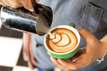 Fototapeta na wymiar Closeup image of male hands barista pouring milk make coffee latte art in coffee shop cafe