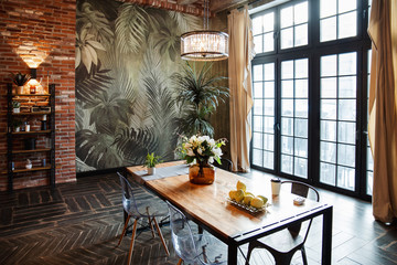 A room with a large window, a table and a wall with branches of flowers.